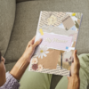 Person holding My Weekly Planner Journal with a floral collage cover while relaxing on a sofa