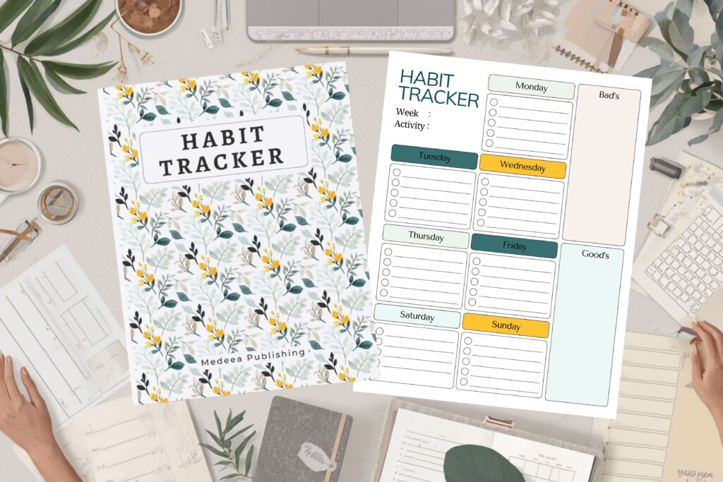 Hardcover habit tracker journal displayed next to an open weekly habit tracking page on a styled desk workspace