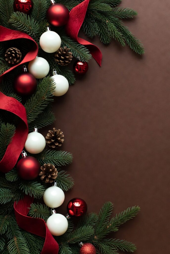 Christmas garland with evergreen branches, red ribbon, ornaments, and pinecones on a dark background.