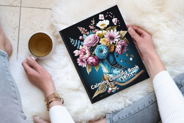 Flowers Bloom Calming Coloring Book Lifestyle Display A physical copy of the Flowers Bloom Calming Coloring Book on a wooden side table next to a cactus.