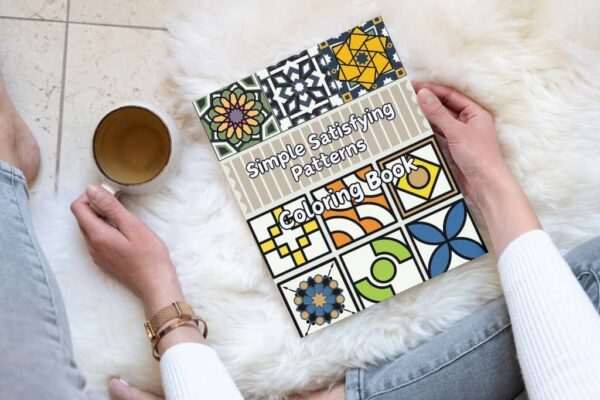 A woman relaxing with the Simple Satisfying Patterns Coloring Book and a cup of tea.