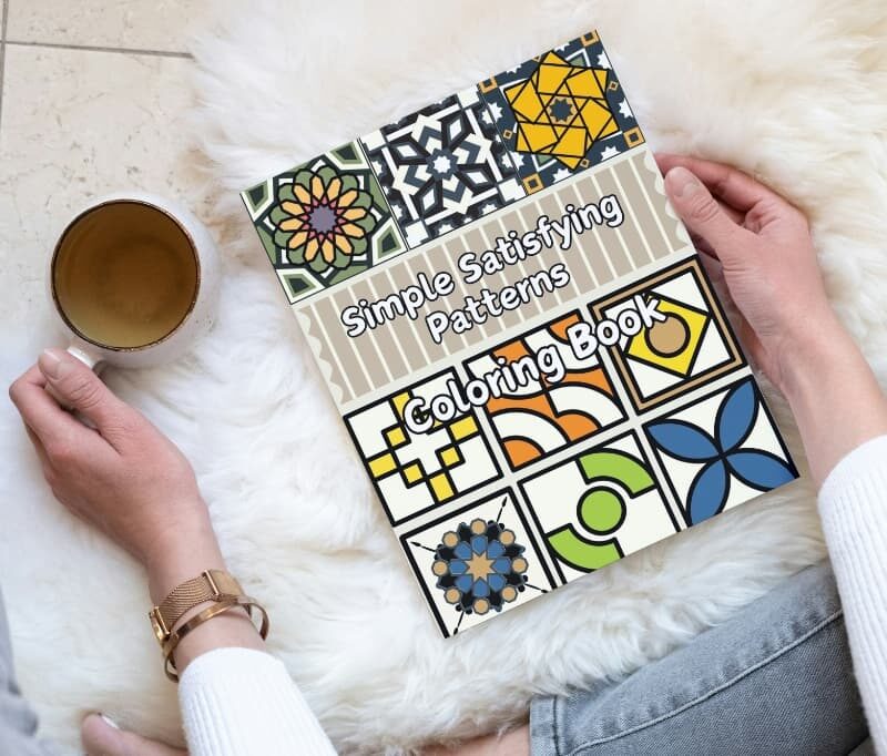 A woman relaxing with the Simple Satisfying Patterns Coloring Book and a cup of tea.