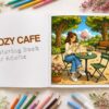 Open cozy cafe coloring book showing a relaxing outdoor park cafe scene with color palette and colored pencils in a bright aesthetic setup
