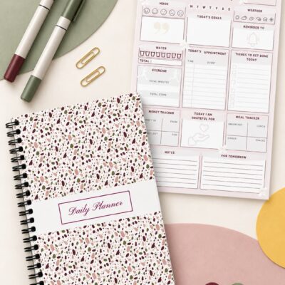 Daily Planner Modern Terrazzo Edition shown in a coil-bound format beside an interior planning page, colorful markers, gold paper clips, and decorative accents.